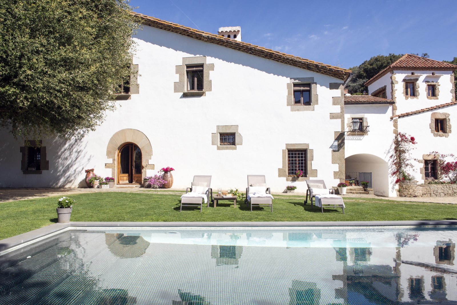 Masia Santa Mònica: façana de pedra blanca amb la piscina i les gandules al jardí